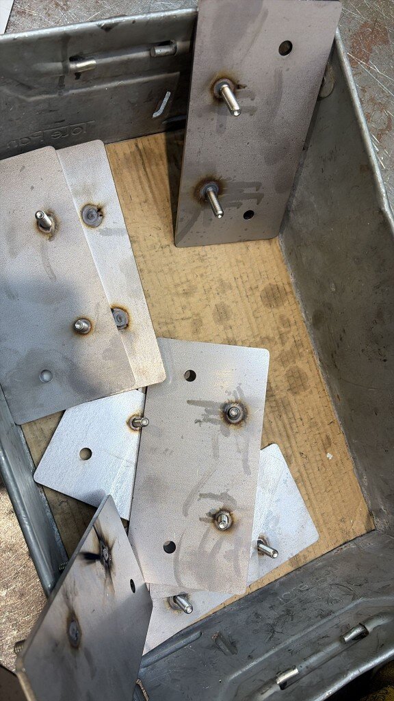 Custom stud plates with welded threaded studs stacked in a workshop parts bin