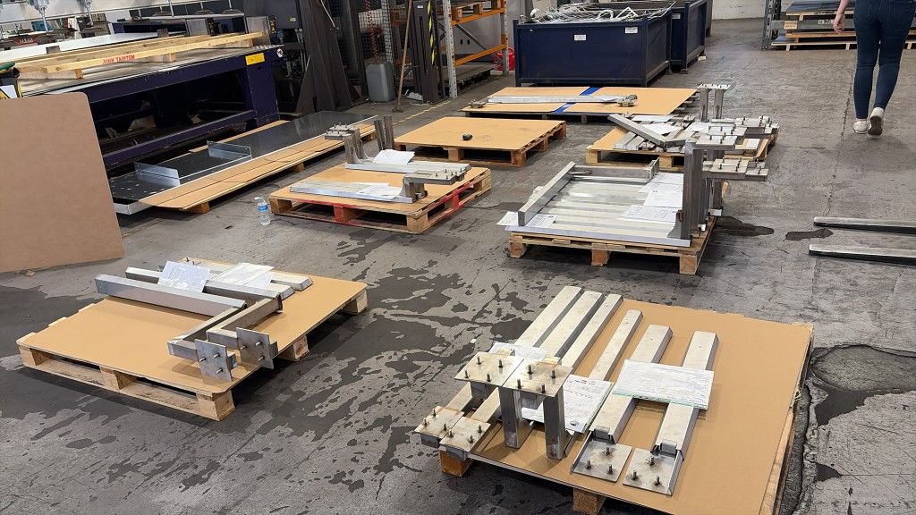 Special-request LoadBear awning brackets lined up across the workshop floor before coating