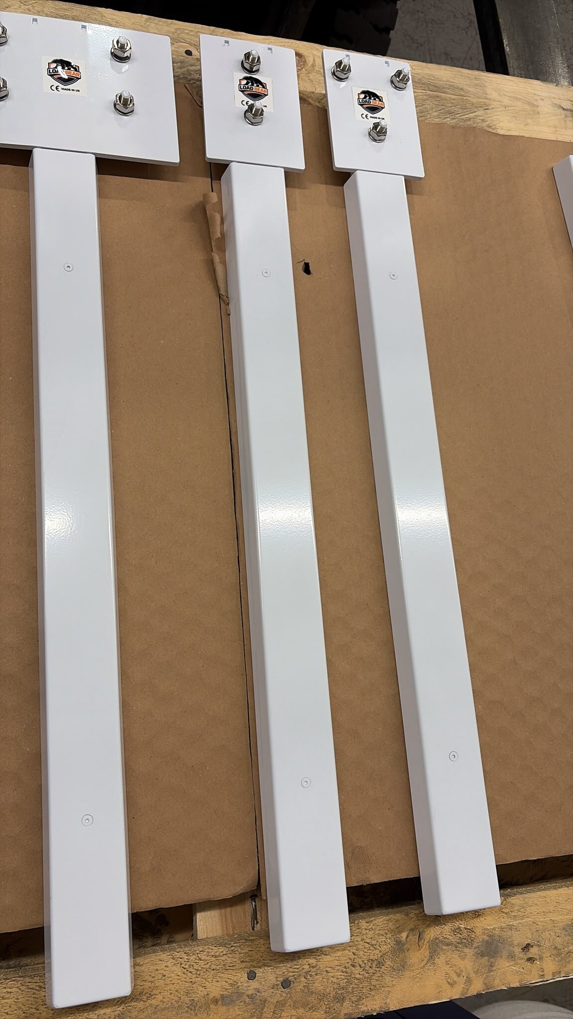 Three white powder-coated LoadBear custom uprights with stud plates on a pallet