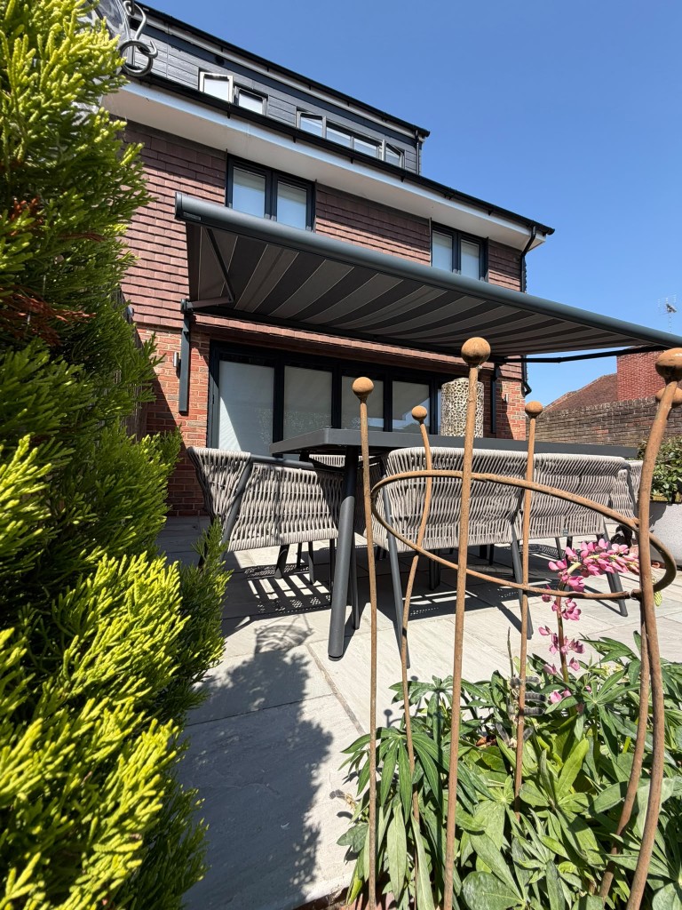 Patio dining under an extended anthracite awning with LoadBear mounts and garden planting