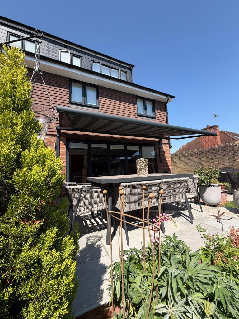 Anthracite BASE awning on LoadBear brackets over a patio dining set