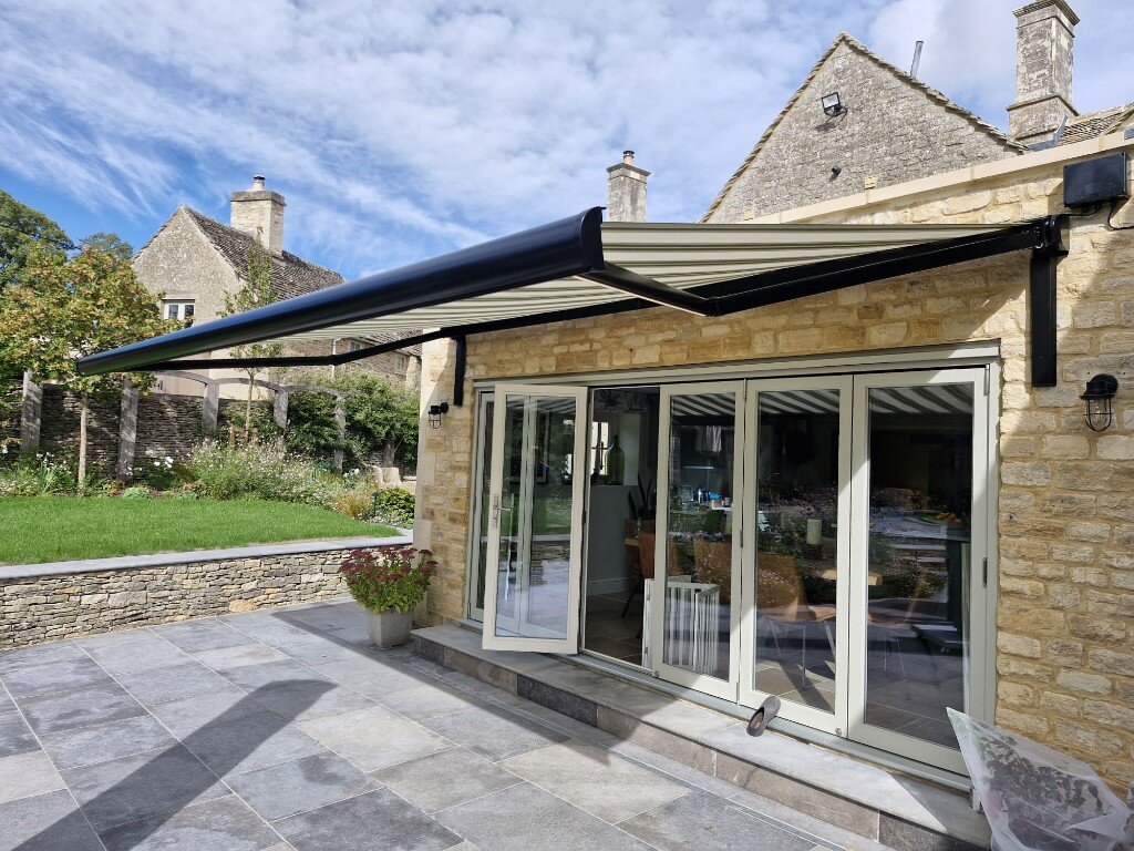 Black BASE awning with striped fabric over bifold doors on a stone house, on LoadBear brackets