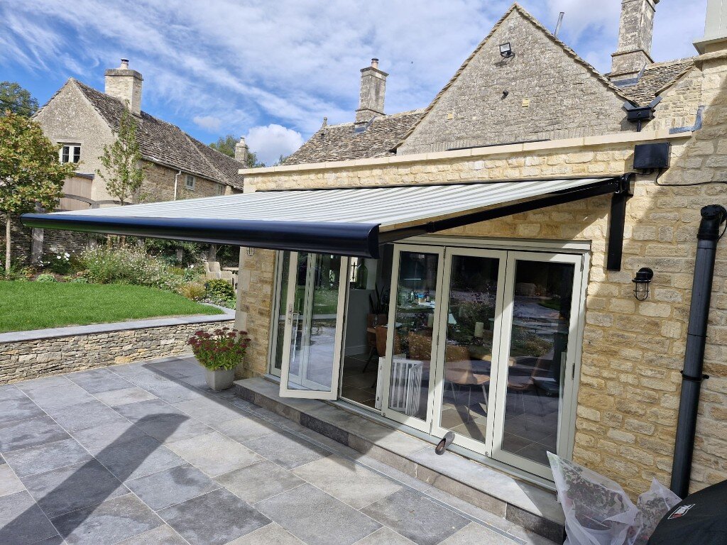 Wide view of a BASE patio awning on LoadBear brackets over grey stone paving