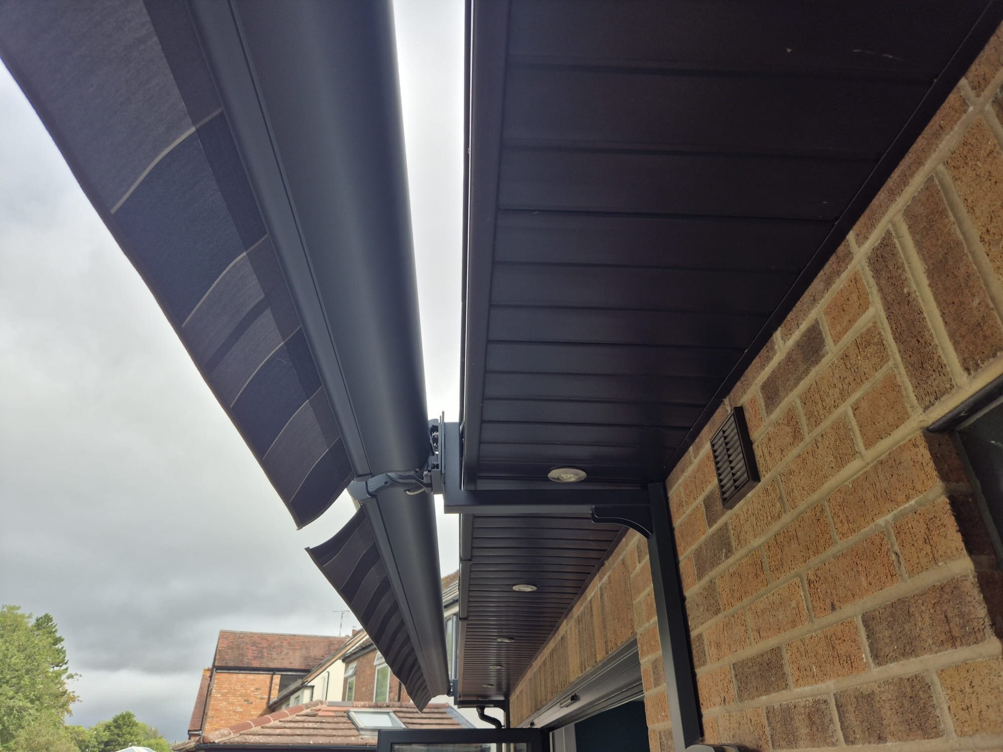 Close-up of a black LoadBear gutter bracket supporting a cassette under a dark soffit