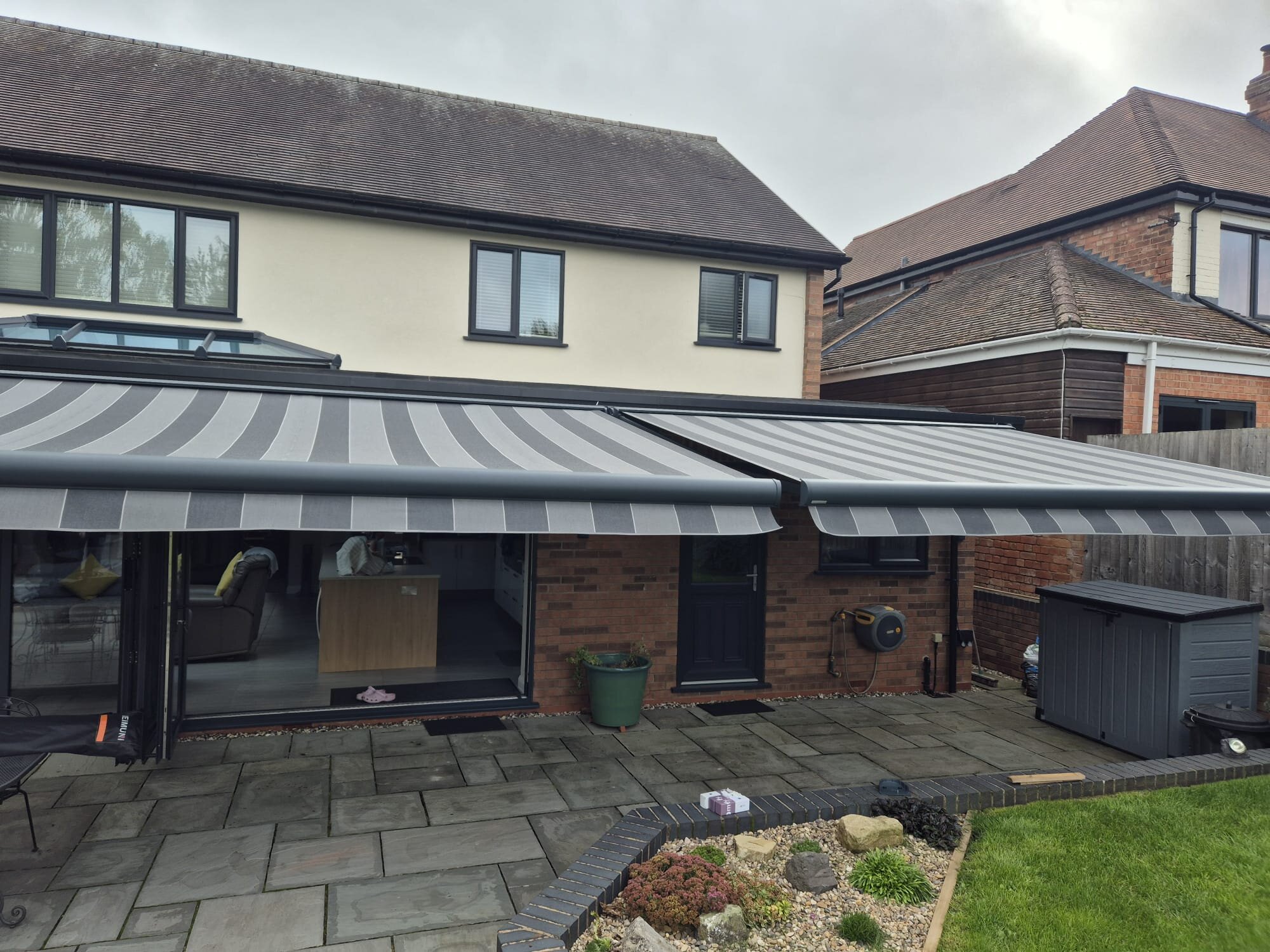 Front view of twin huge awnings on LoadBear gutter brackets over grey patio paving