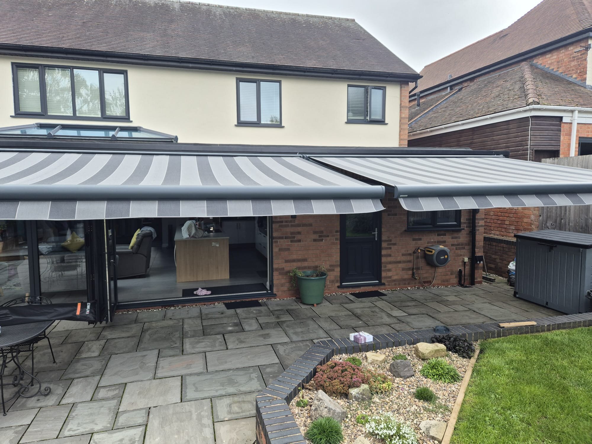 Two huge striped cassette awnings extended over a brick patio on LoadBear gutter brackets