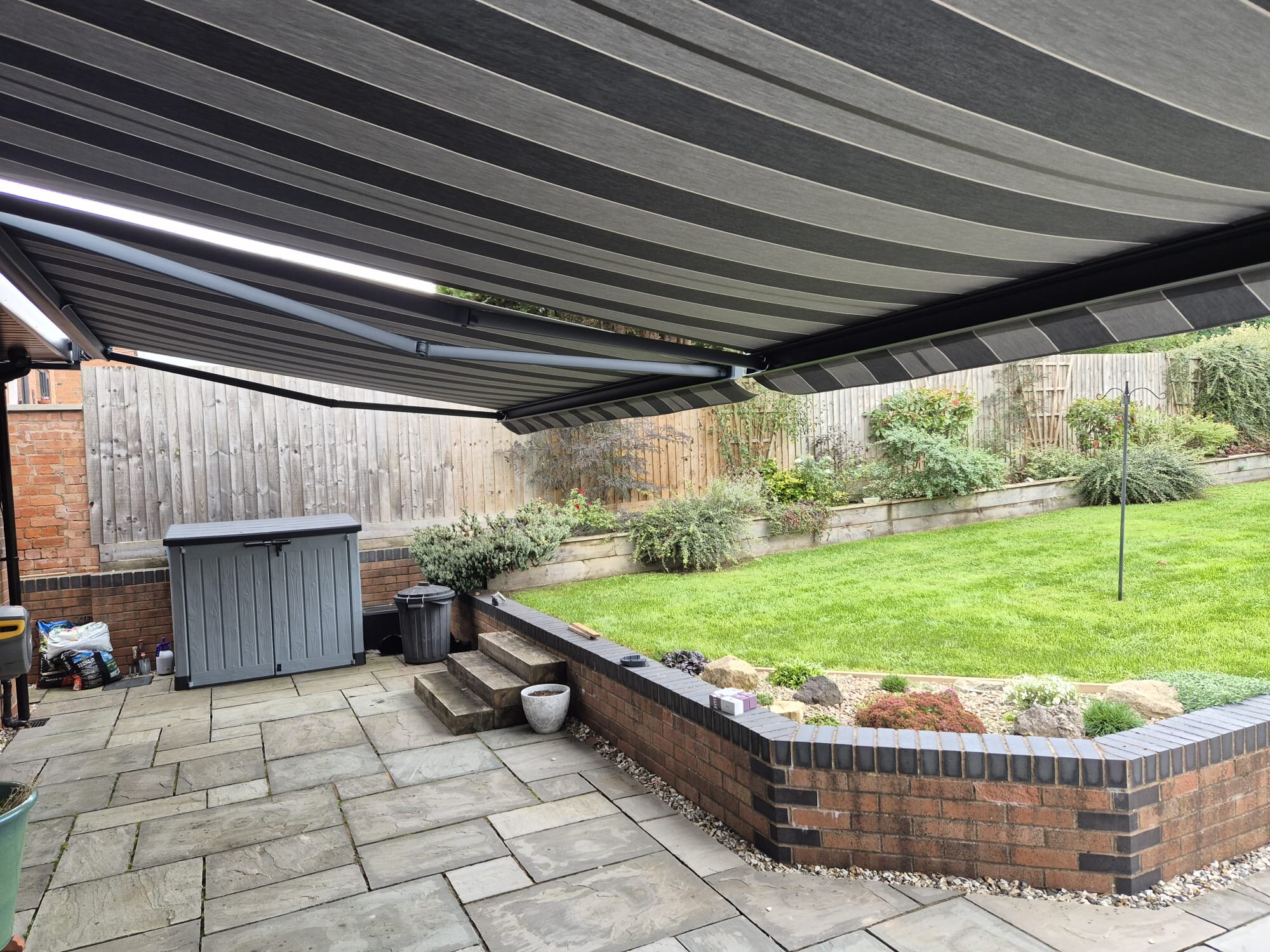 Under-canopy view of a huge awning with LED strip over a stone patio garden