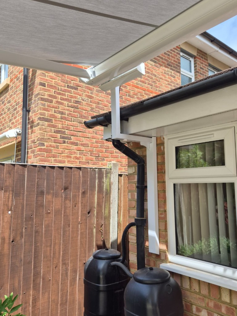 Close-up of white LoadBear gutter bracket on red brick next to a black downpipe